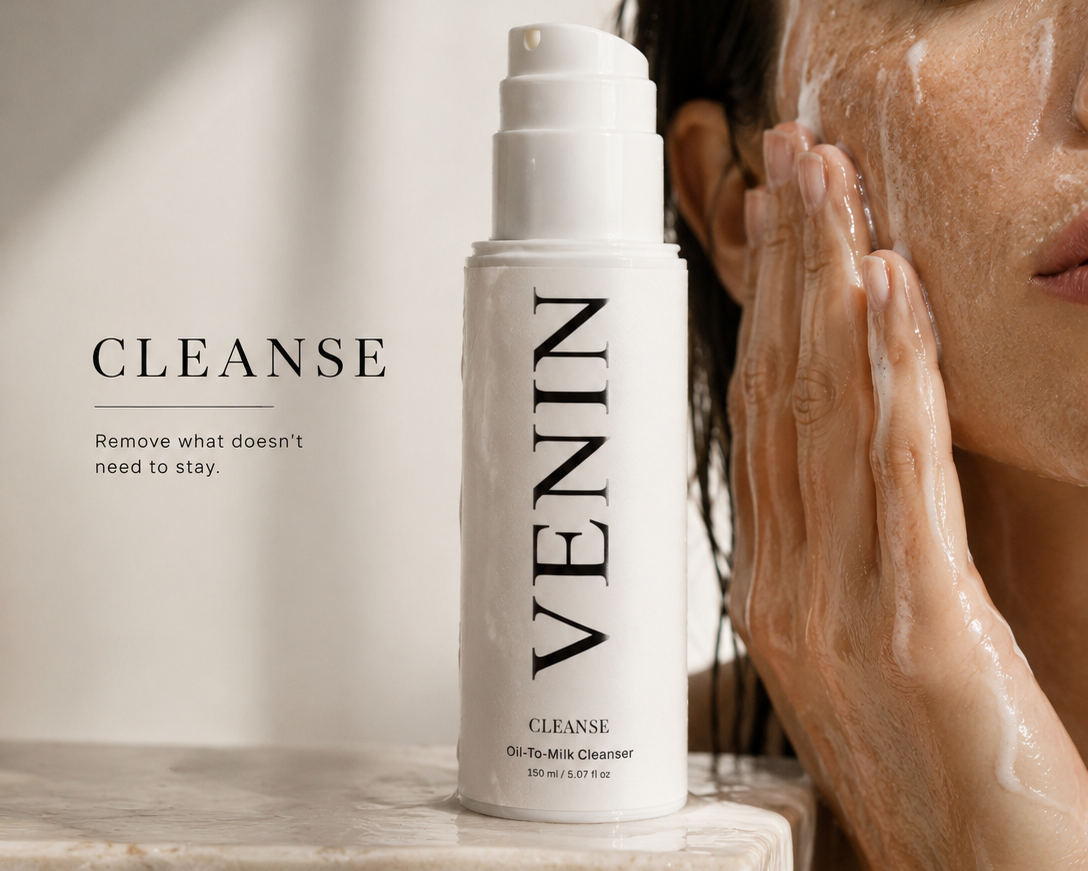 VENIN Cleanse oil skin cleanser bottle displayed on a marble ledge next to a woman washing her face with foamy cleanser, in a bright, sunlit setting.