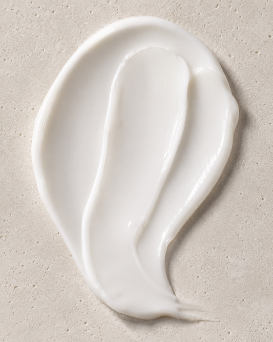 A thick, creamy white lotion smear on a textured beige stone surface.