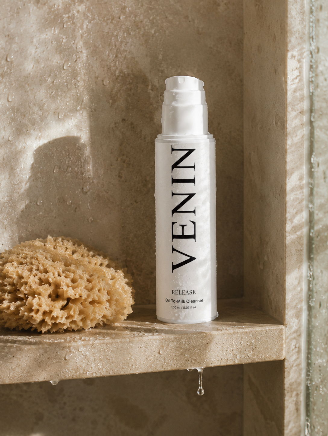 VENIN Release Hyalu Cleanser bottle standing on a stone shelf next to a natural loofah sponge, with water droplets and warm directional light.