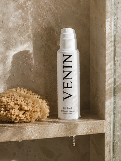 VENIN Release Hyalu Cleanser bottle standing on a stone shelf next to a natural loofah sponge, with water droplets and warm directional light.