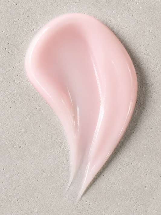 A smooth, glossy smear of pale pink cream or lotion on a textured light gray surface.